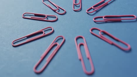 close up of pink paper clips arranged on blue background, in slow motion