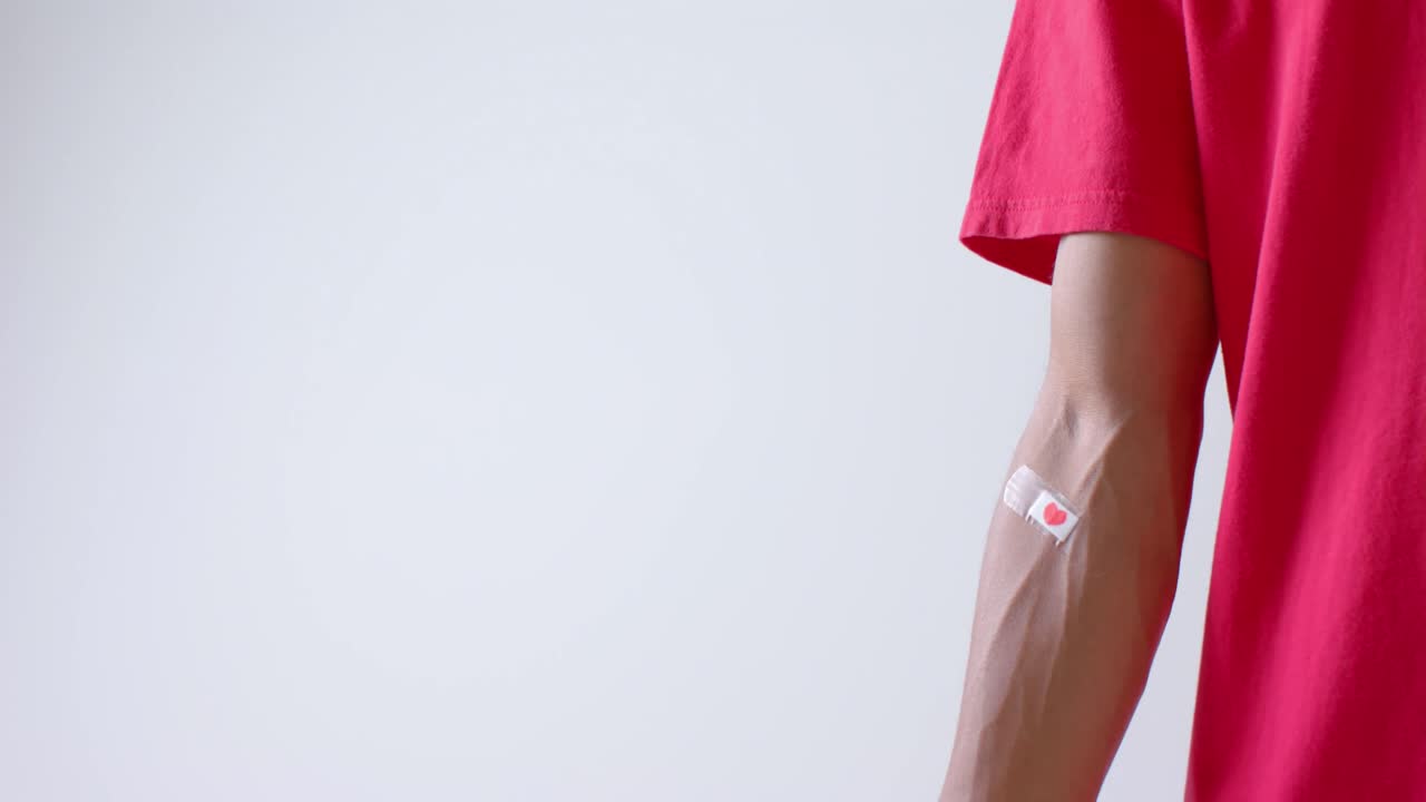 sección media de un hombre biracial con el corazón pegando yeso en el brazo, en blanco con espacio de copia, cámara lenta