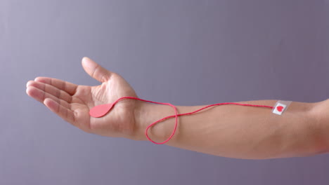 mano de hombre biracial con gota de sangre, cuerda roja y corazón pegando yeso en gris, cámara lenta