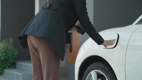 progressive woman installing plug from home charging station to electric vehicle