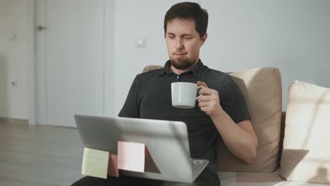 hombre trabajando desde casa en una computadora portátil, bebiendo café