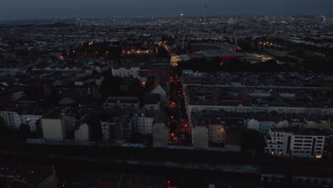 Aerial-view-of-morning-cityscape-with-Fernsehturm-TV-tower.-Tilt-down-view-of-street-in-residential-neighbourhood-modestly-lit-by-street-lights.-Berlin,-Germany