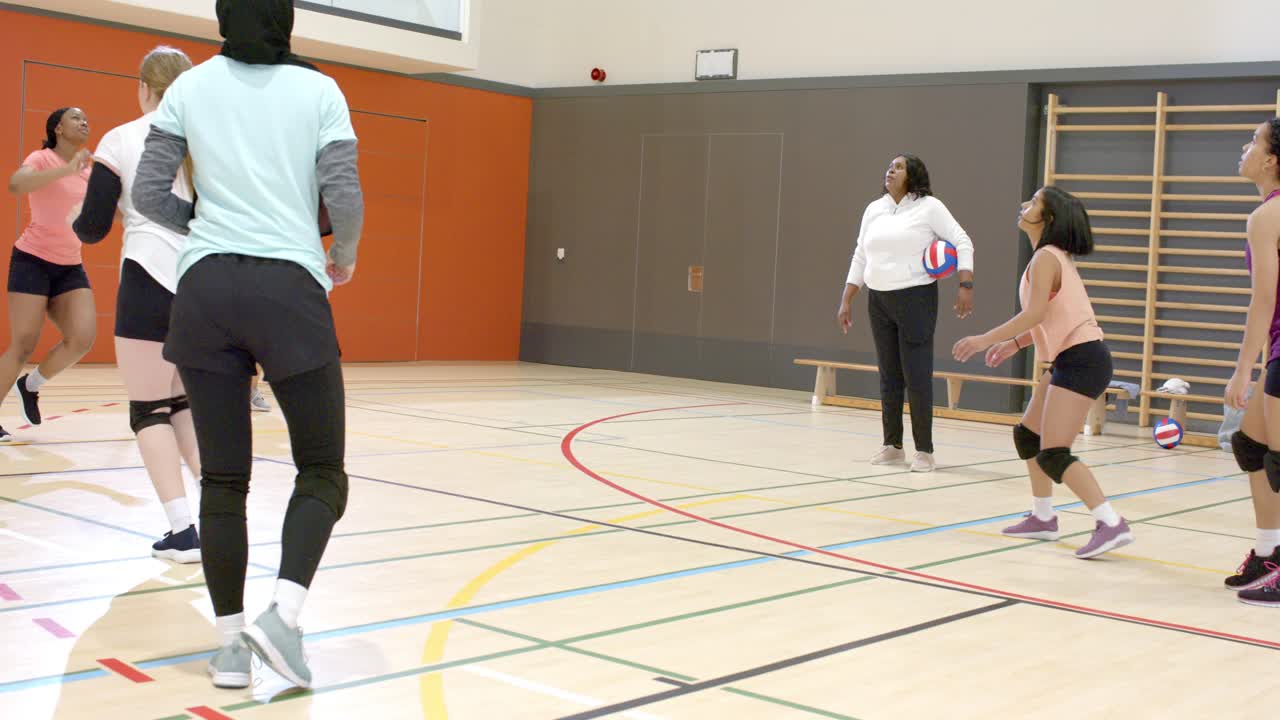 Équipe féminine diverse s'entraînant aux manchettes et aux passes après que l'entraîneur ait lancé le ballon de volley-ball sur le terrain, avec espace pour le texte.