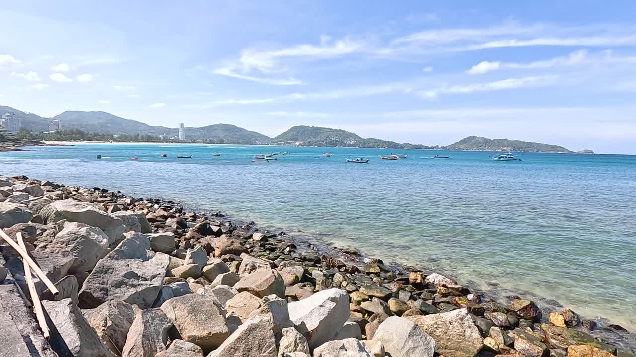 A tranquil scene of Kalim Beach's rocky shoreline with clear blue waters and distant hills under a bright sky