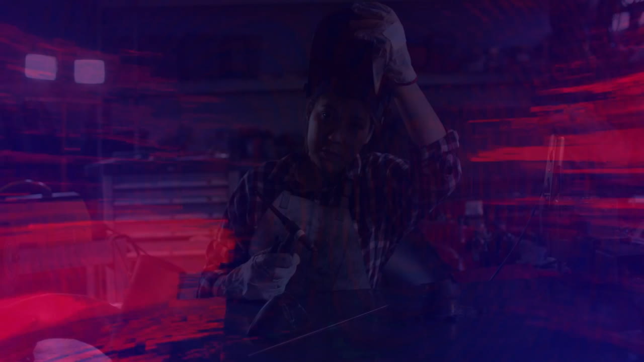 Metalworker woman adjusting hair while holding grinder in metal workshop, animating red streaks