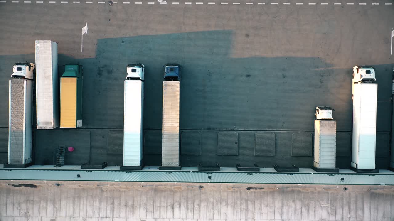 많은 트럭이 상품을 하역하고 있는 산업 창고 보관 건물 적재 구역을 떠나는 세미 트레일러가 부착된 트럭의 항공 샷