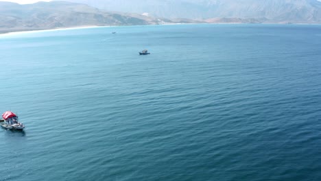 A-sunny-day-on-Socotra-island-in-Yemen,-with-fishing-boats-dotting-the-ocean-waves-against-a-stunning-mountain-backdrop