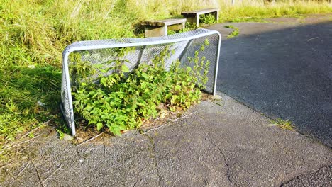 Ein-Reichlich-Buschiger,-Ungenutzter-Torpfosten-Auf-Dem-Betonboden-An-Einem-Hellen,-Sonnigen-Tag,-Aufgrund-Einer-Covid-Sperre