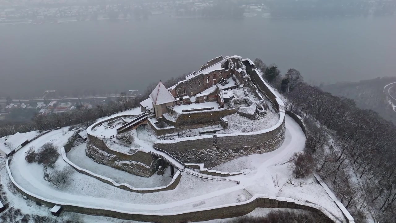 I Visegrád står de snötäckta slottsruinerna Fellegvár på en bergstopp ovanför Donau mitt bland Visegrádbergen, visat i ett brett vinterlandskap fångat av en drönare.