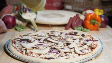 primer plano de manos de un chef experto rociado con aceite de oliva sobre masa de pizza con champiñones frescos, queso mozzarella y salsa roja jugosa