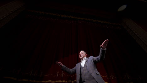 theatrical man on stage. performer in a suit moving on stage on red curtains background. professional actor performing in theater. view from below.