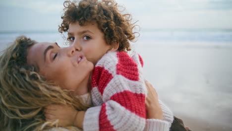 happy mother cuddling son at autumn ocean shore closeup. sincere family emotions