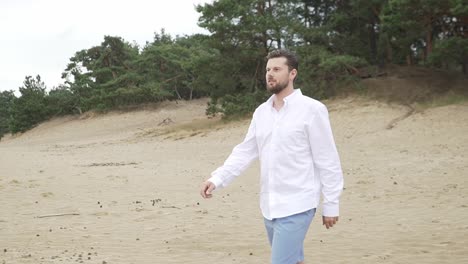 a man walking out of the forest on a sandy beach in slow motion