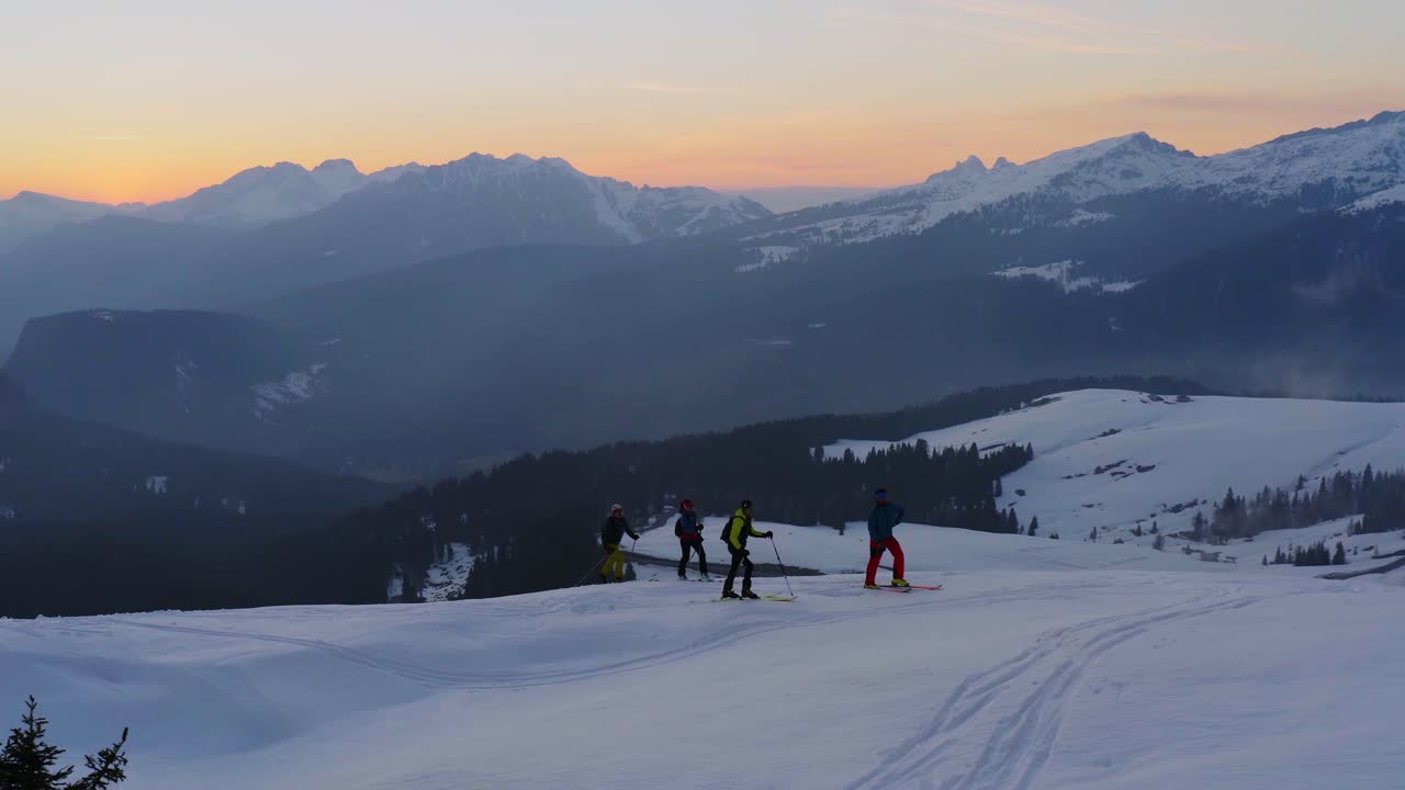 Un gruppo di sci alpinisti scala la cima innevata del Passo Rolle al tramonto.