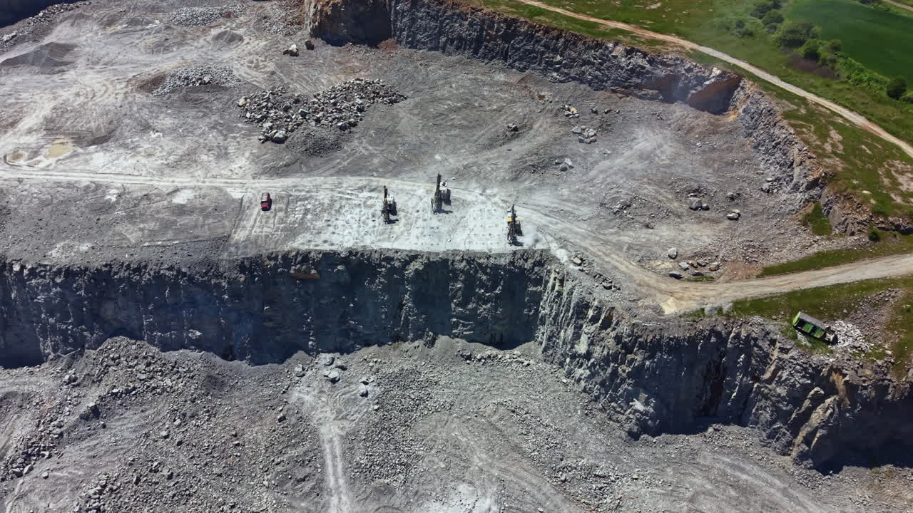 Mining activity takes place in a large quarry with excavators and trucks working on a rock surface during a sunny day