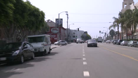 Ein-Auto-Fährt-Eine-Straße-In-Venedig-Kalifornien-Entlang,-Gesehen-Durch-Die-Heckscheibe-1