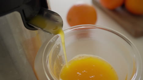 jugo de naranja fresco vertido en un vaso desde el exprimidor a un vaso con telón de fondo de fruta