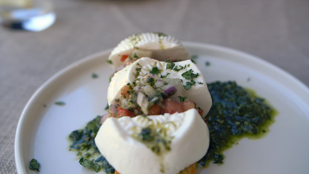 Slow motion footage showing a plate of bruschetta topped with Gozo cheese, chopped tomatoes, onions and pesto