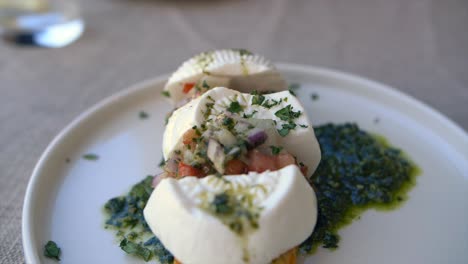 slow motion footage showing a plate of bruschetta topped with gozo cheese, chopped tomatoes, onions and pesto
