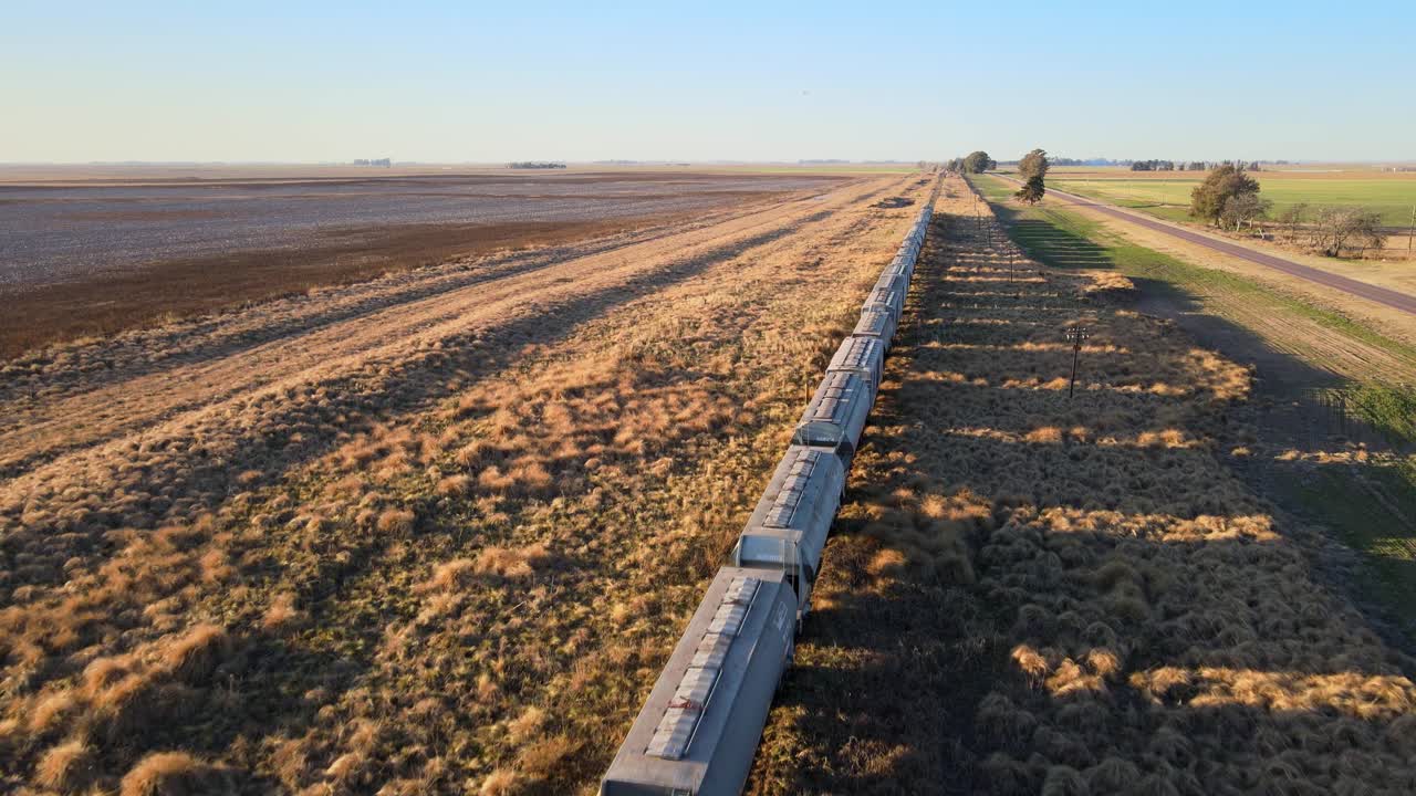 Drone dolly against direction of freight train carrying grain across the flatlands of La Pampa, Argentina, for export
