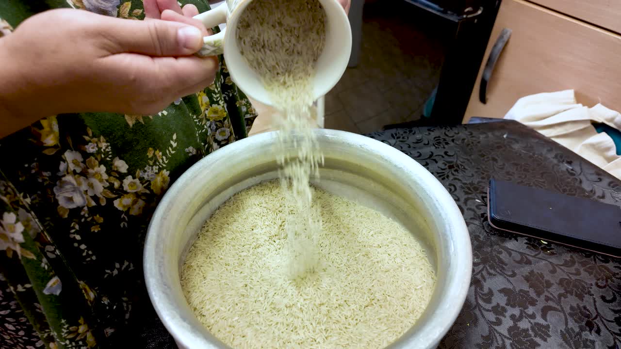 Housewife pouring dry rice from cup into pot, preparing ingredients for cooking