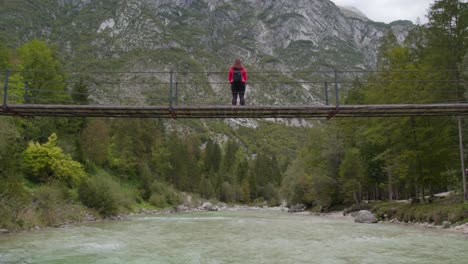 Drone-flies-toward-suspension-bridge-above-a-calm-Soca-river,-aerial