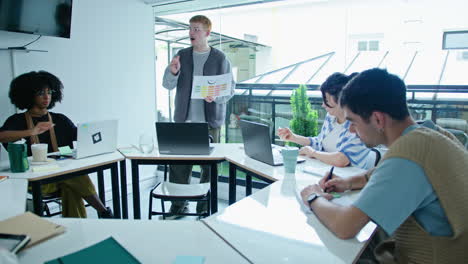 gen z man explaining business graphs on paper to colleagues on meeting