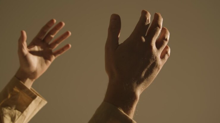 Studio Close Up Shot Of Man Wearing Robes Raising Hands In Prayer