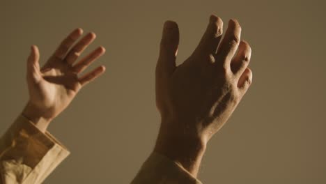 studio close up shot of man wearing robes raising hands in prayer