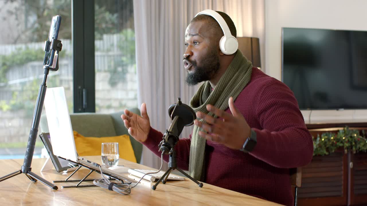 Mid adult African American man donning headphones gesturing into microphone at desk for emphasis