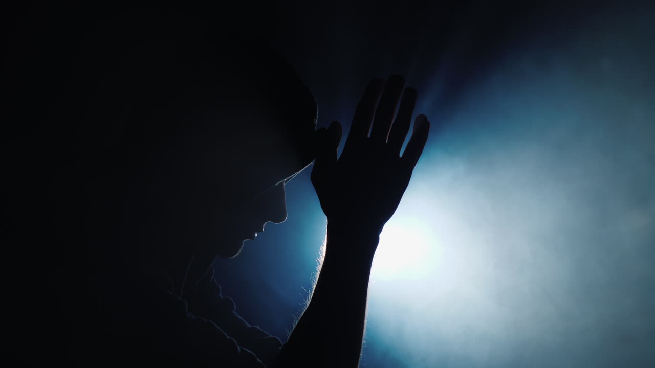 silueta de un hombre encapuchado rezando en la oscuridad