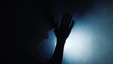 silhouette of a man in a hood praying in the dark