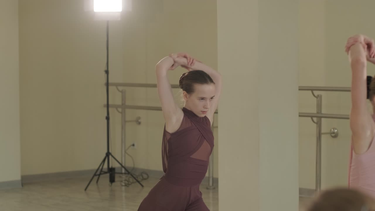 группа молодых студентов балета в черной танцевальной одежде практикует позиции в просторной балетной студии с деревянным полом и настенными решетками. сосредоточенные выражения и синхронизированные движения.