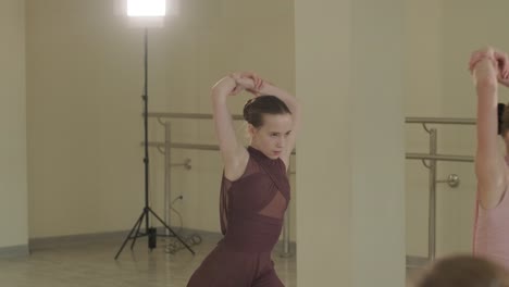 un grupo de jóvenes estudiantes de ballet con ropa de baile negra practicando posiciones en un amplio estudio de ballet con pisos de madera y barras montadas en la pared. expresiones enfocadas y movimientos sincronizados.