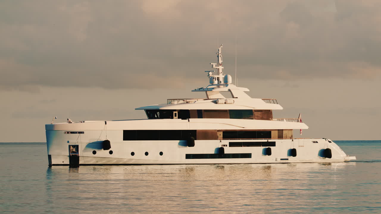 Vista laterale di un moderno yacht di lusso che solca le acque calme del mare con un faro in lontananza