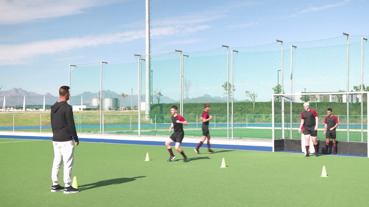 Running hockey drill, male athletes training on field with coach observing