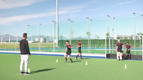 running hockey drill, male athletes training on field with coach observing