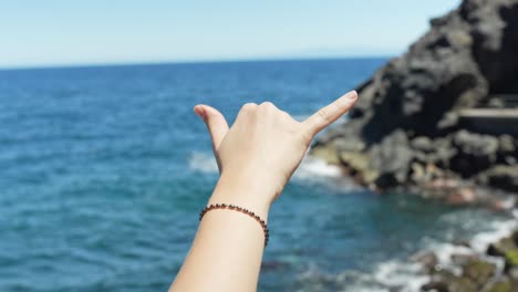 person hand showing cool gesture near rocky ocean coastline, pov