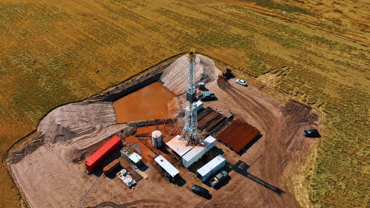 Site for oil production in the desert field. High derrick for drilling resources in the center of the location. Top view.