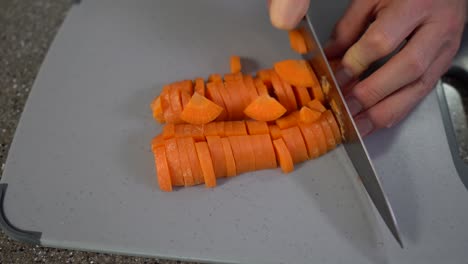 man hands cutting the carrot into small pieces with chefs knife on grey chopping board on the table, top view