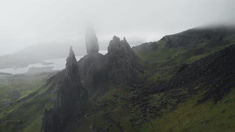 Drone-shot-backwards-movement-of-old-man-of-storr-landscape-in-isle-of-skye-scotland,-cloudy-day-and-green-grass