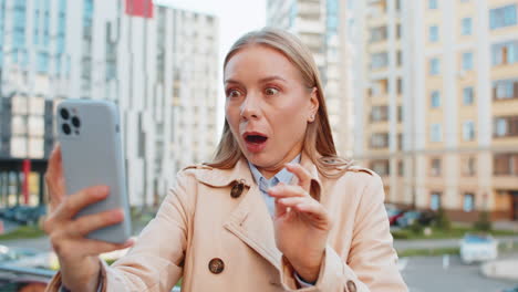 caucasian mature woman looking shocked while reading good news on smartphone on downtown city street