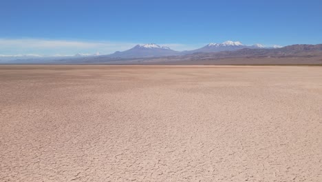 high-altitude drone shot over the atacama desert salt flat, showing salt, earth, and lithium crusts under daylight, with snow-capped andes mountains in the background.