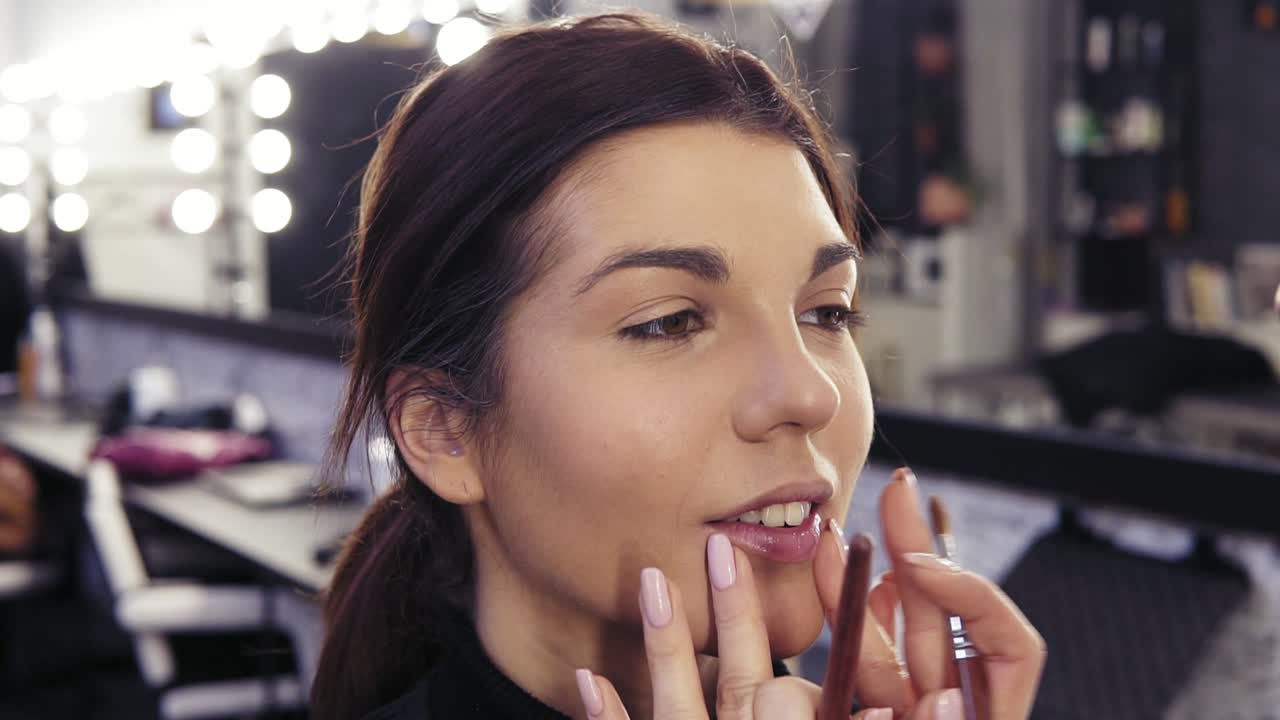 Gorgeous young brunette girl with hazelnut eyes has concealer applyed by make up artist on her chin area. Creating stunning flawless look.