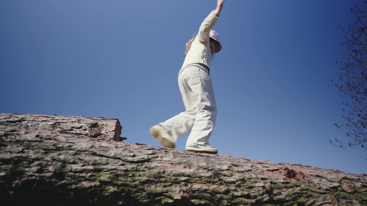 The girl balances carefully on a pile of logs. Low angle shot.