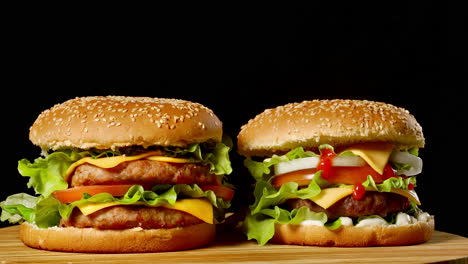 two craft beef burgers on wooden table isolated on dark grayscale background.