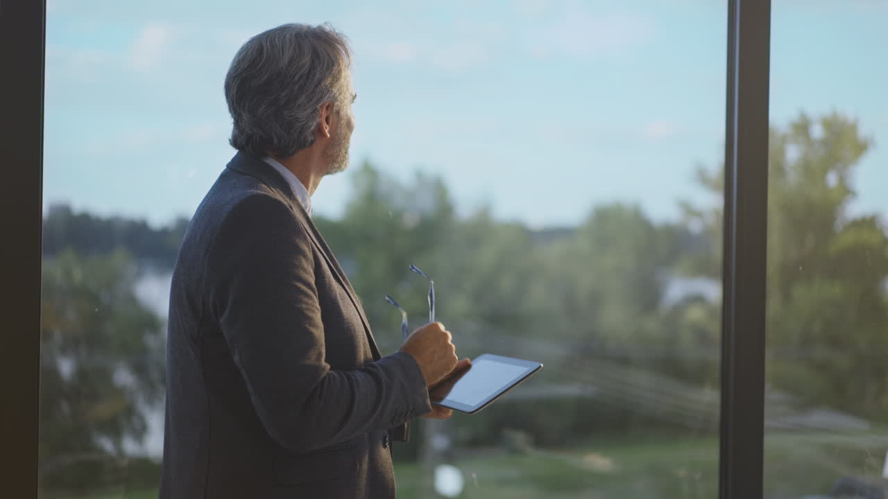 태블릿을 가진 창문을 통해 보는 고위 사업가