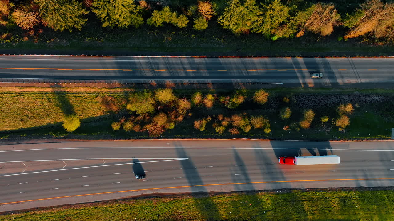 Lorries and trucks ride by the two-lane highway. Transport throwing long shadows on the road at sunset. Top view.