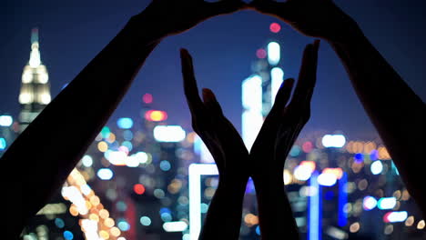 hands forming heart at night over a city