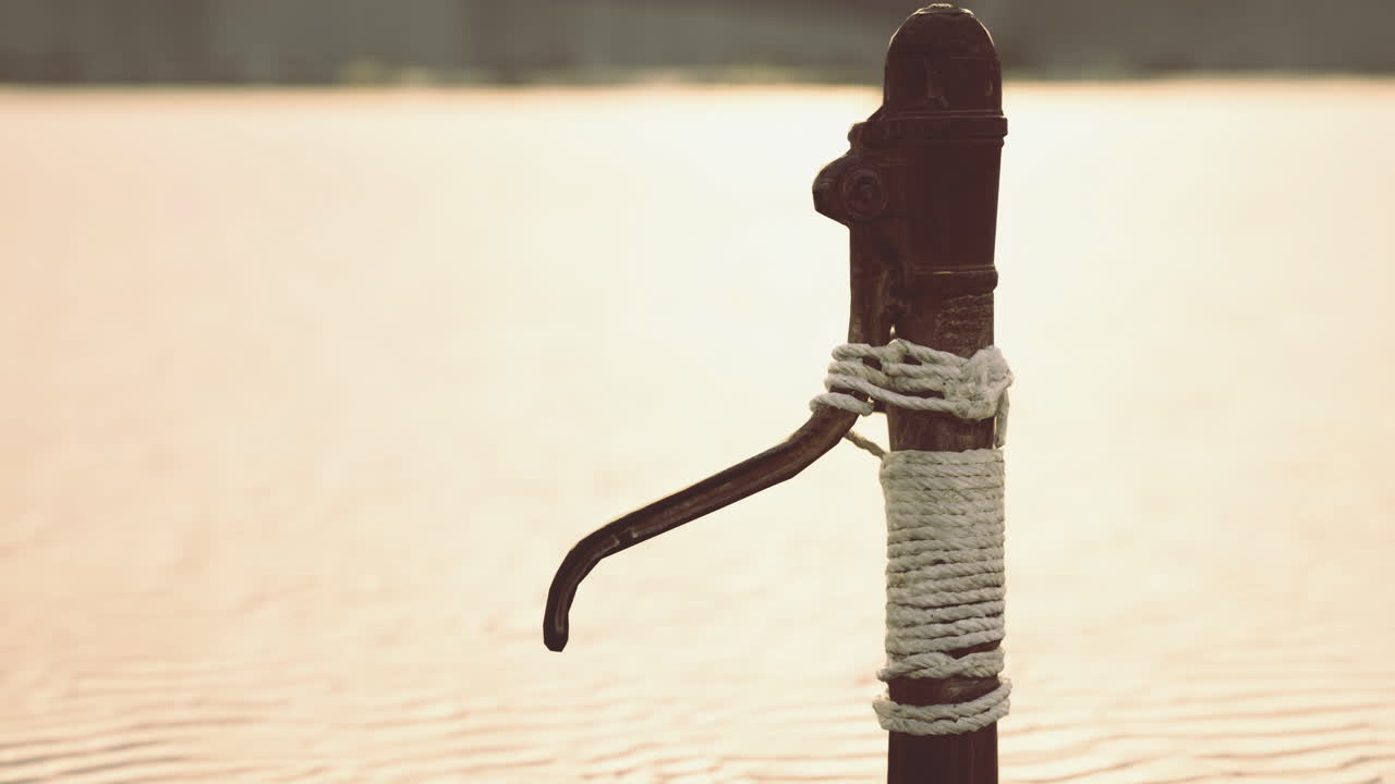 Old hand pump by tranquil waters at sunset in rural area